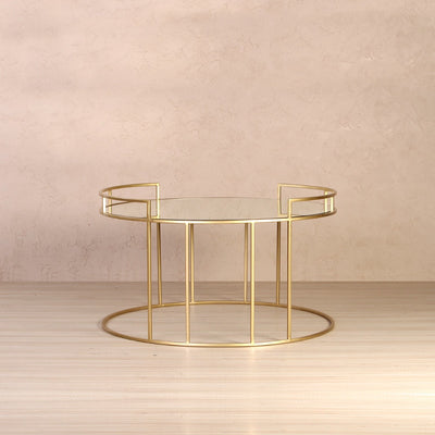 Round coffee table with glass top supported by metal legs in gold finish 