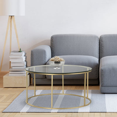 Round coffee table with glass top supported by metal legs in gold finish