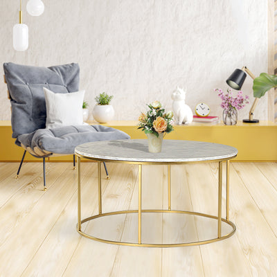 Round coffee table with natural white marble top supported by metal legs in gold finish